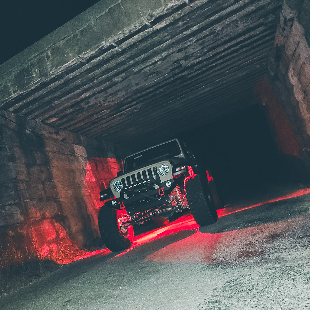 Shackles hanging on front bumper of Jeep Gladiator with red under glow driving through a tunnel 